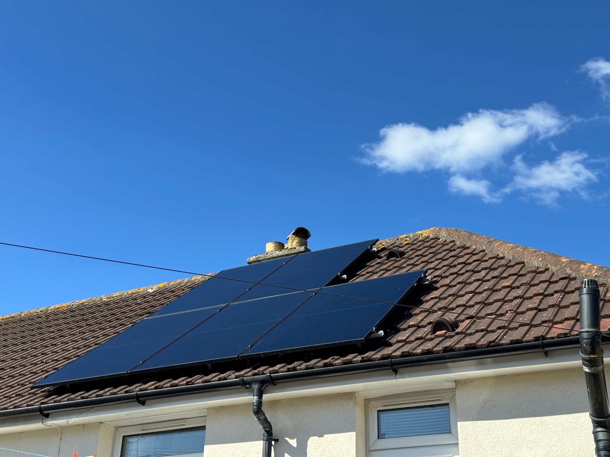 Eight black solar panels fitted to the tiled roof of a house under a blue sky
