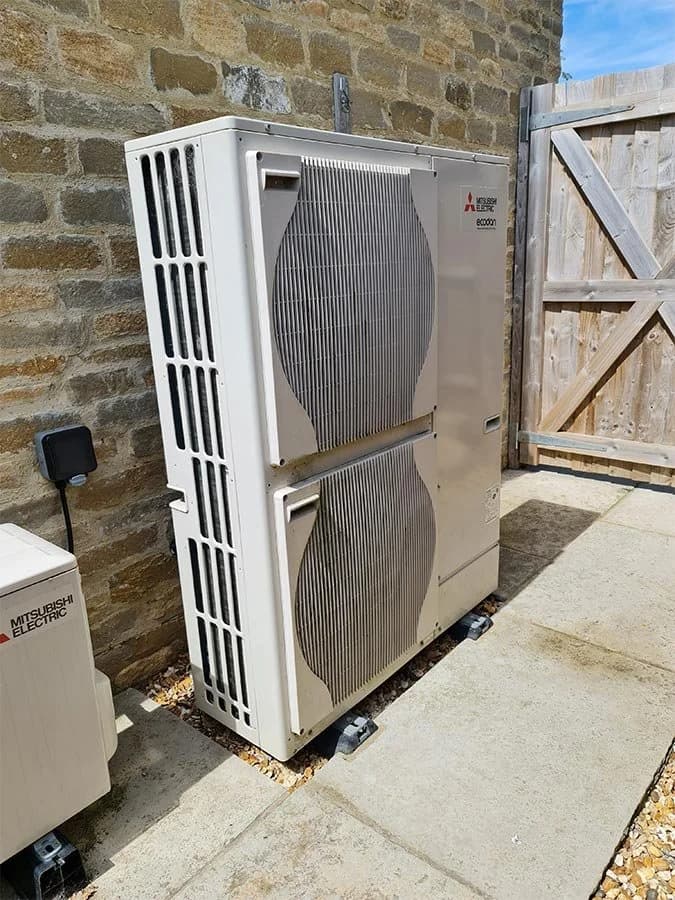 A tidy air source heat pump installation beside a traditional UK brick or stone home.