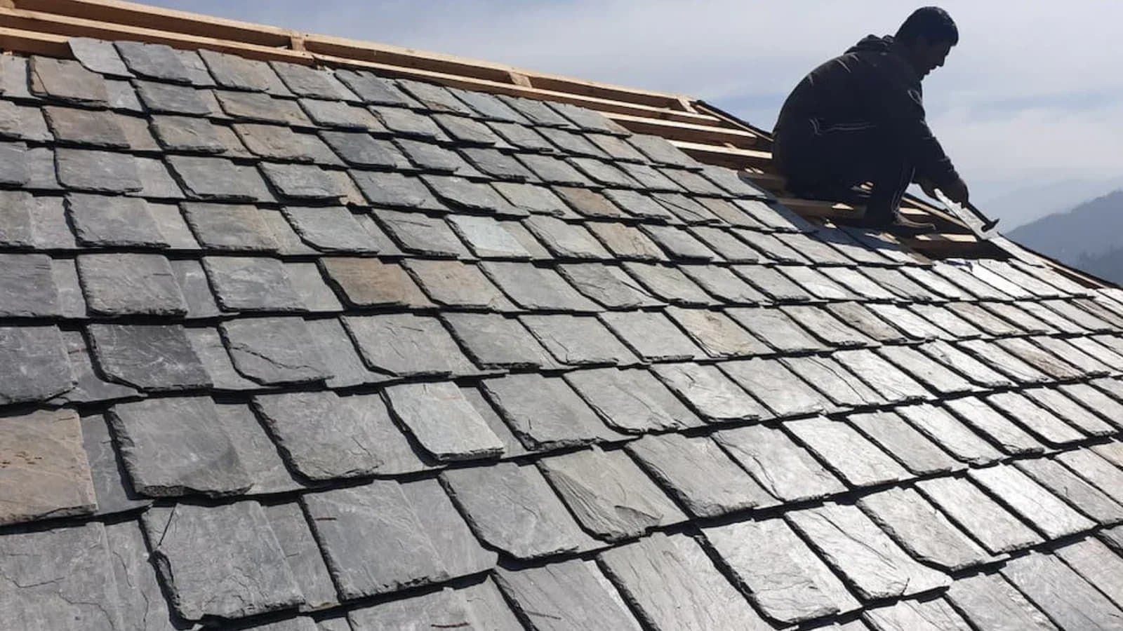Slate roof tiles with a roofer working near the ridge.