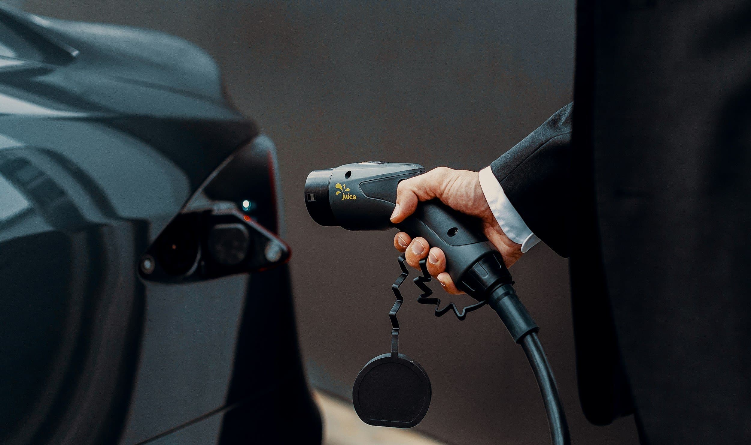 Person holding an EV charging connector next to an electric car’s charging port.