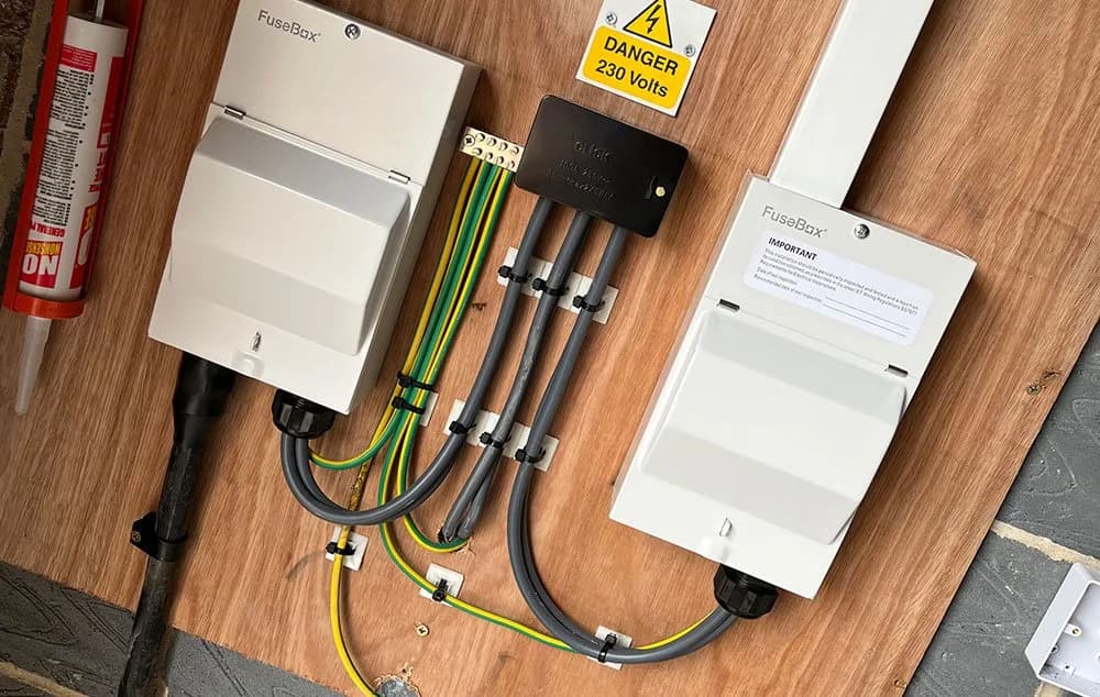 Two FuseBox electrical isolator units mounted on a board with conduit, earthing cables, and a “Danger 230 Volts” warning sign.