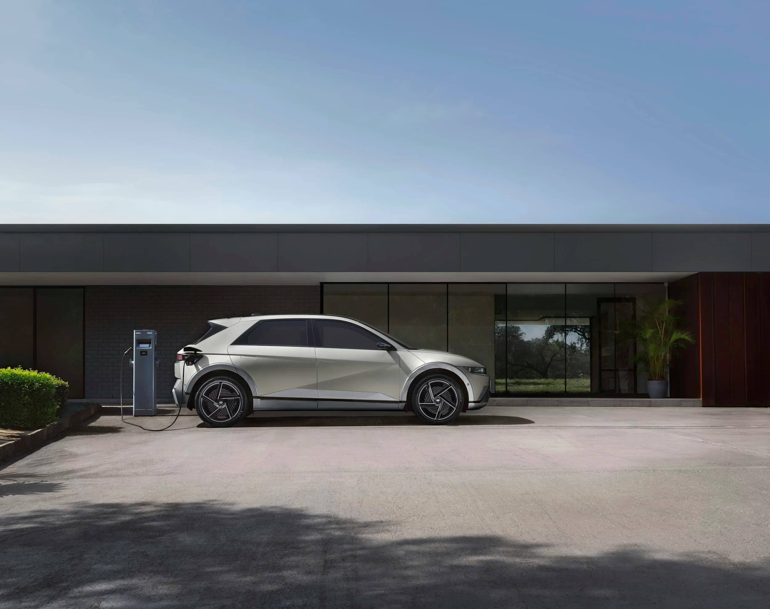 White Hyundai Ioniq 5 electric SUV parked and connected to a DC fast charging station in front of a modern building with large glass windows on a sunny day.