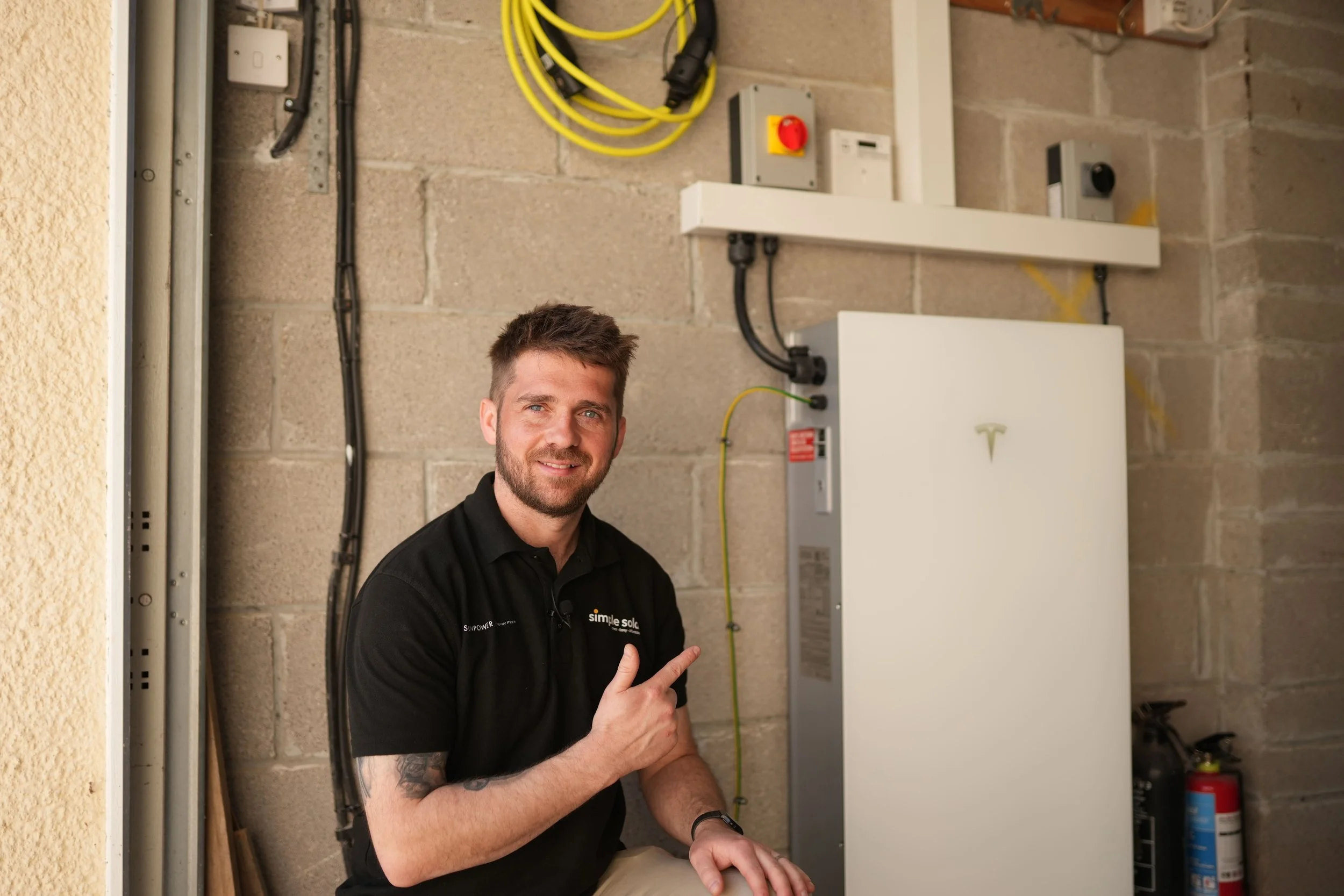 A Simple Solar installer beside a Tesla Powerwall 3 home battery fitted in a garage