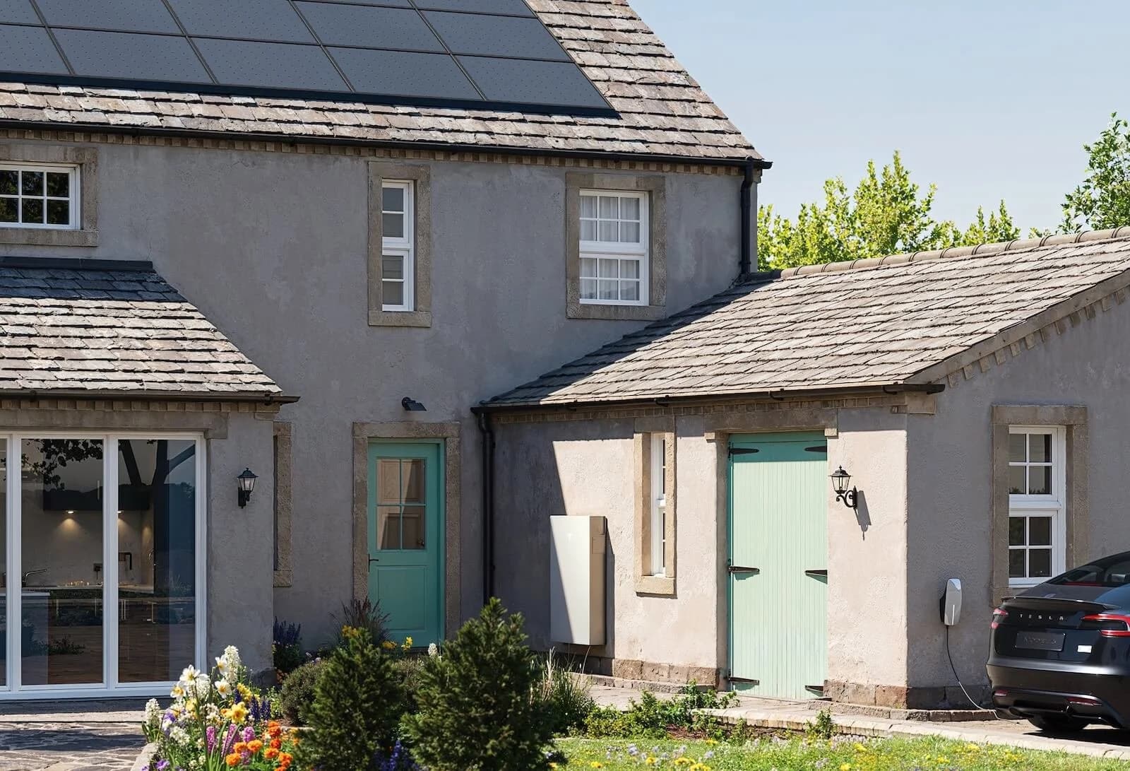 A stone cottage with solar panels on the roof and a Tesla Powerwall home battery on the outside wall
